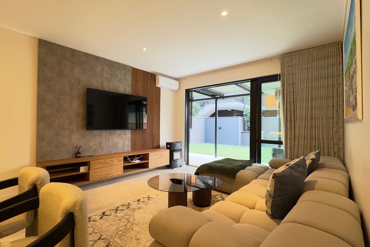 Modern living room featuring a custom media wall with slatted wood and concrete-effect finishes, air conditioning, and large sliding doors opening to the patio.