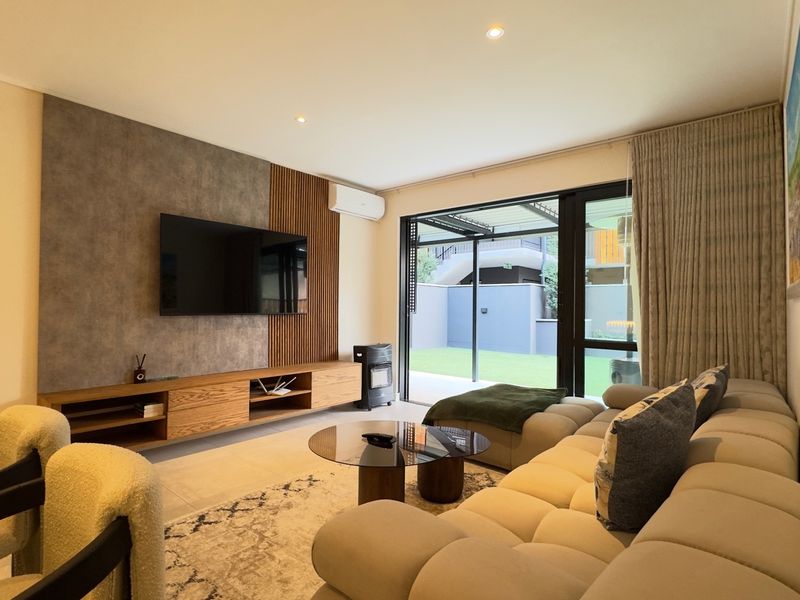Modern living room featuring a custom media wall with slatted wood and concrete-effect finishes, air conditioning, and large sliding doors opening to the patio.