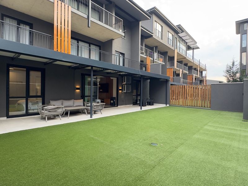A modern ground-floor apartment featuring a covered patio area and a private artificial lawn garden with contemporary architectural finishes.