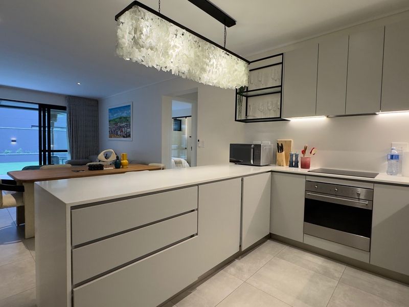 Modern open-plan kitchen featuring sleek cabinetry, stone countertops, and integrated appliances, flowing seamlessly into the dining and living area with access to the patio.
