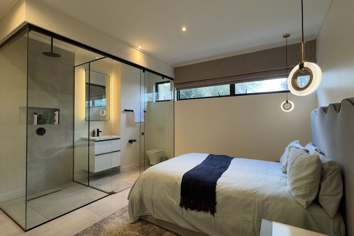 Modern bedroom featuring an open-concept glass-enclosed ensuite bathroom with a wall-mounted vanity and walk-in shower, complemented by contemporary lighting and neutral finishes.