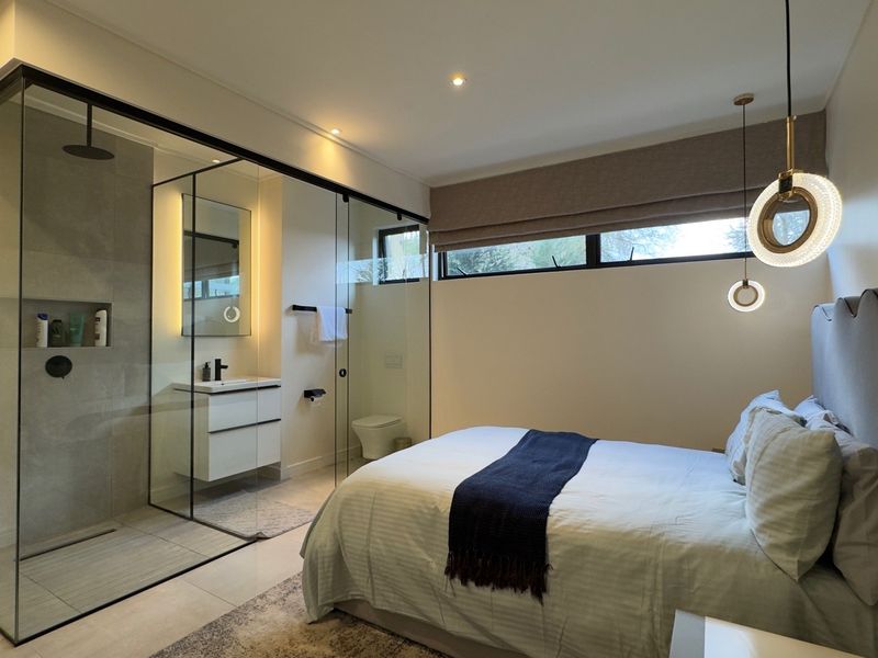 Modern bedroom featuring an open-concept glass-enclosed ensuite bathroom with a wall-mounted vanity and walk-in shower, complemented by contemporary lighting and neutral finishes.