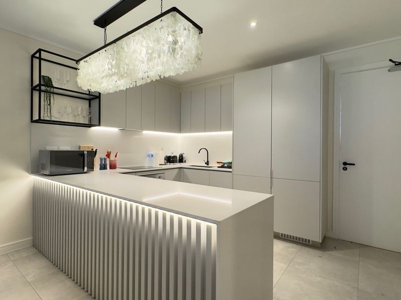Modern kitchen featuring sleek handleless cabinetry, quartz countertops, a slatted breakfast bar with integrated lighting, and high-quality finishes throughout.