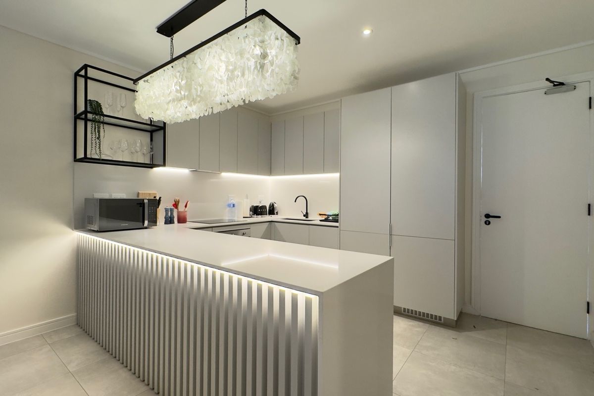 Modern kitchen featuring sleek handleless cabinetry, quartz countertops, a slatted breakfast bar with integrated lighting, and high-quality finishes throughout.