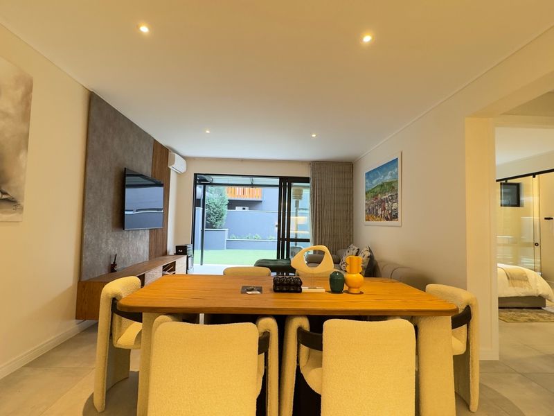 A bright open-plan living and dining area featuring tiled floors, recessed lighting, and sliding glass doors leading to an outdoor patio space.