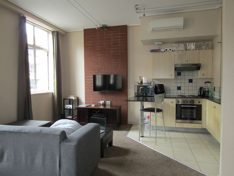 Open-plan living area featuring a kitchen with built-in appliances, tiled flooring, and a distinct exposed brick feature wall with an integrated air conditioning unit.