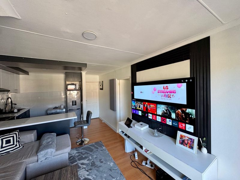 Open-plan living area featuring a compact kitchen with breakfast bar, laminate flooring, and a dedicated media wall with decorative paneling.