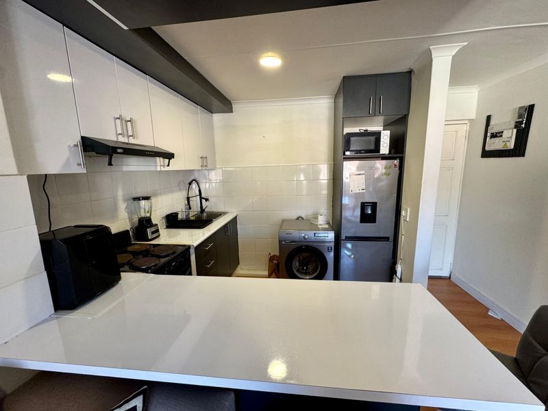 A functional kitchen featuring white and dark cabinetry, a breakfast bar, tiled backsplash, and integrated appliance housing, offering a clean and modern aesthetic.