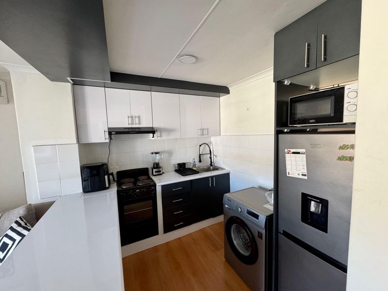 Compact kitchen featuring modern two-tone cabinetry, built-in electric stove with extractor, tiled backsplash, and integrated space for laundry appliances.