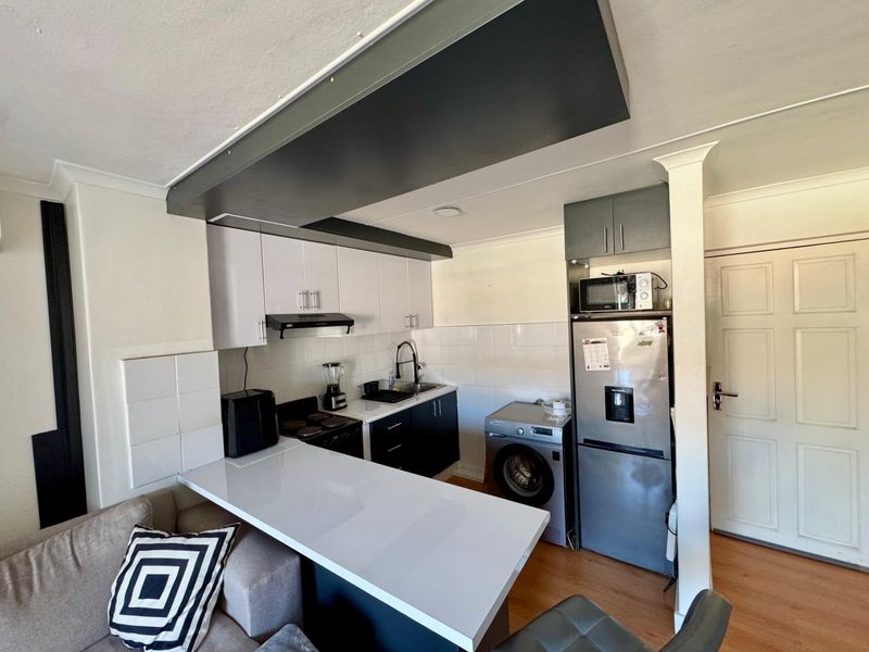 Compact kitchen featuring modern two-tone cabinetry, white tiled backsplash, integrated breakfast bar, and laminate flooring in an open-plan layout.