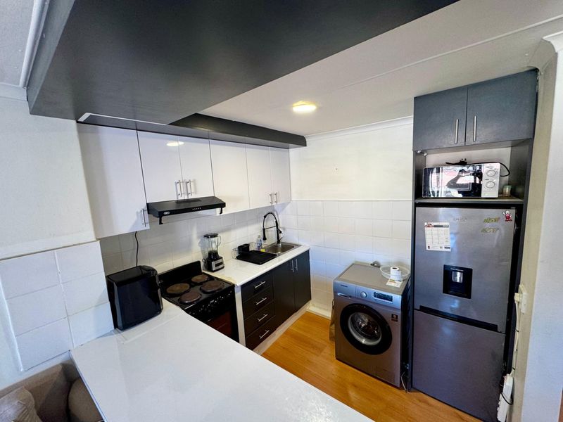 Compact kitchen featuring modern two-tone cabinetry, electric stove, extractor fan, and integrated laundry space with tiled backsplash and laminate flooring.