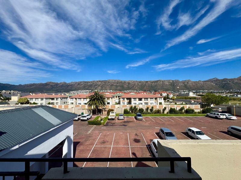 Elevated view overlooking the apartment complex parking area with scenic mountain vistas in the background.