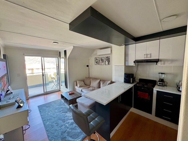 Open-plan living area featuring a modern kitchen with built-in cabinetry, electric stove, and direct access to a private balcony through sliding glass doors.