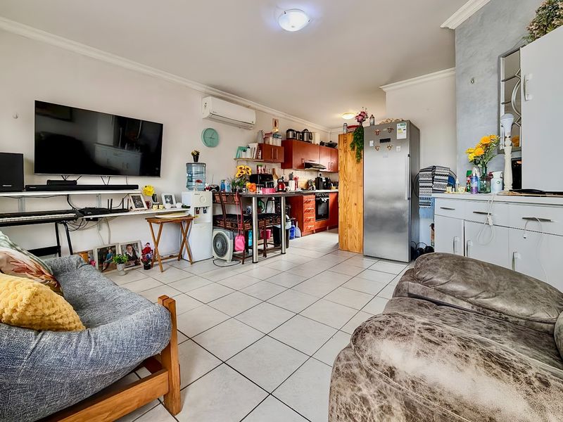 Open-plan living area featuring tiled floors, a functional kitchen with built-in cabinetry, and a wall-mounted air conditioning unit.