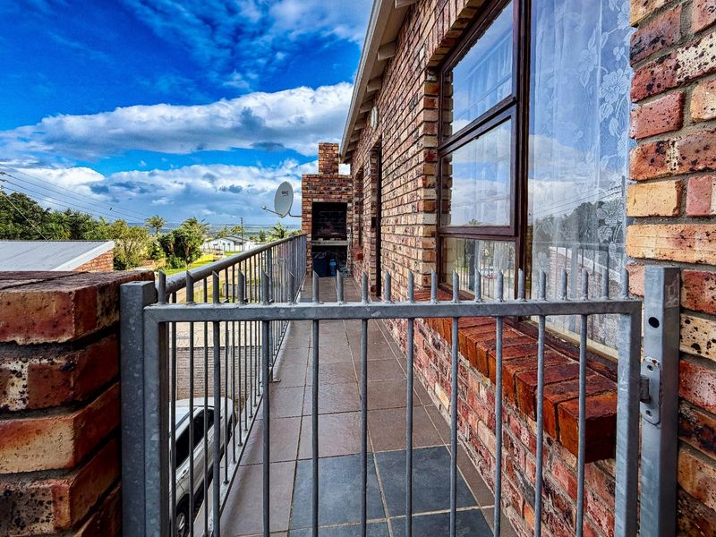 A brick-finished balcony featuring tiled flooring, a built-in braai, and metal security railings, offering an elevated outdoor space.