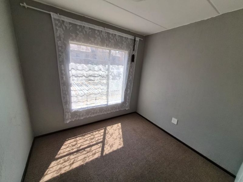 An empty bedroom featuring neutral grey walls, carpeted flooring, and a large sliding window allowing for natural light.