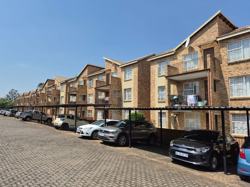 Exterior view of a multi-story apartment complex featuring face brick construction, private balconies, and dedicated covered parking bays for residents.