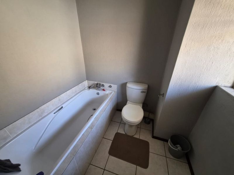 A functional bathroom featuring a built-in bathtub and toilet with tiled flooring, presenting a dated aesthetic suitable for modernization.