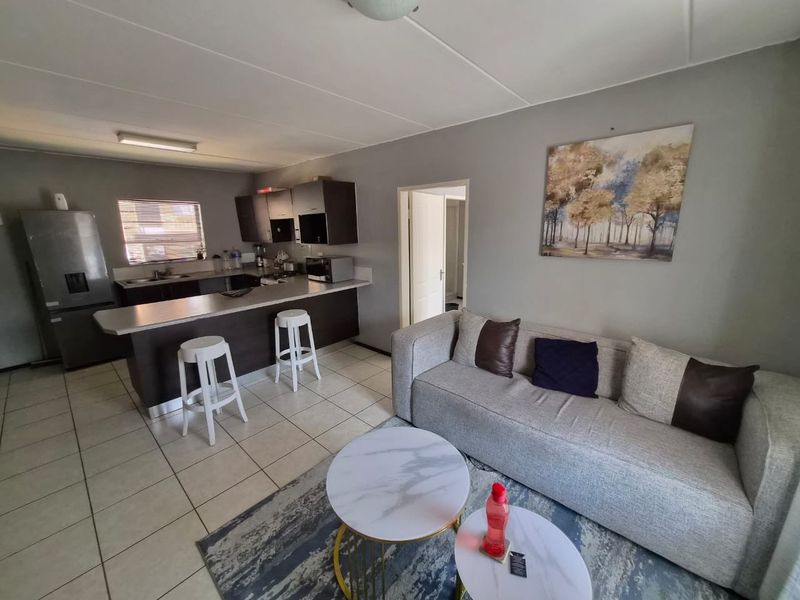 An open-plan living area featuring a functional kitchen with a breakfast bar, tiled flooring, and a comfortable lounge space.