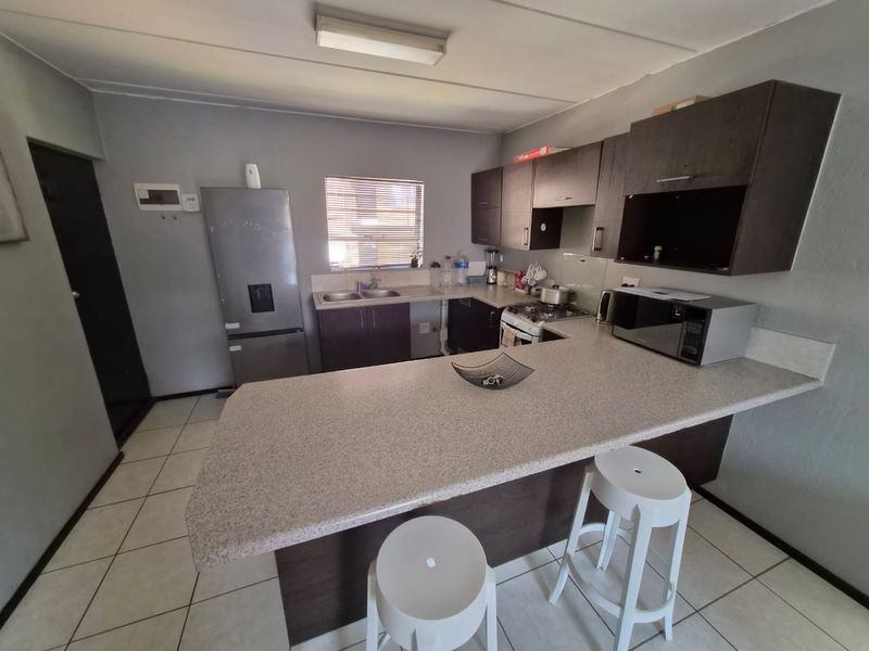 Functional kitchen featuring dark cabinetry, laminate countertops, a breakfast bar, and tiled flooring, providing a practical layout for daily meal preparation.