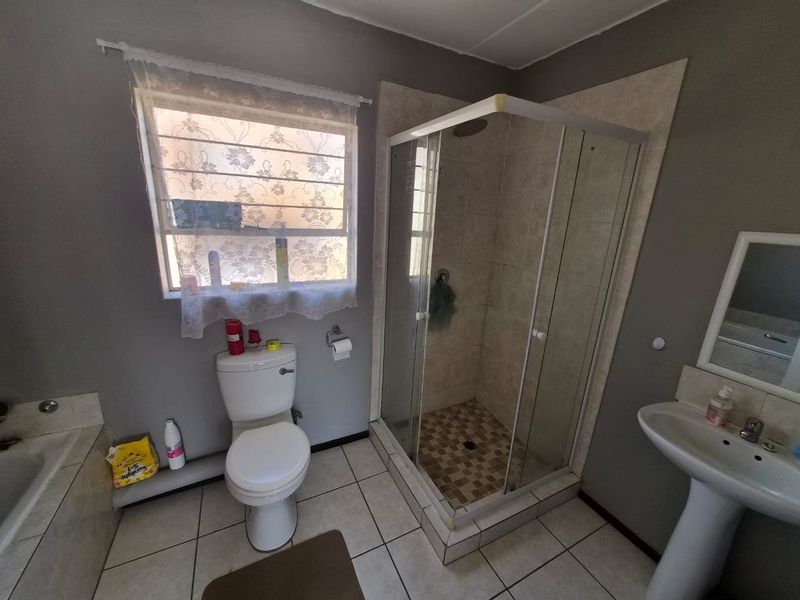 A functional bathroom featuring a glass-enclosed shower, pedestal basin, and toilet, with tiled flooring and neutral wall finishes.