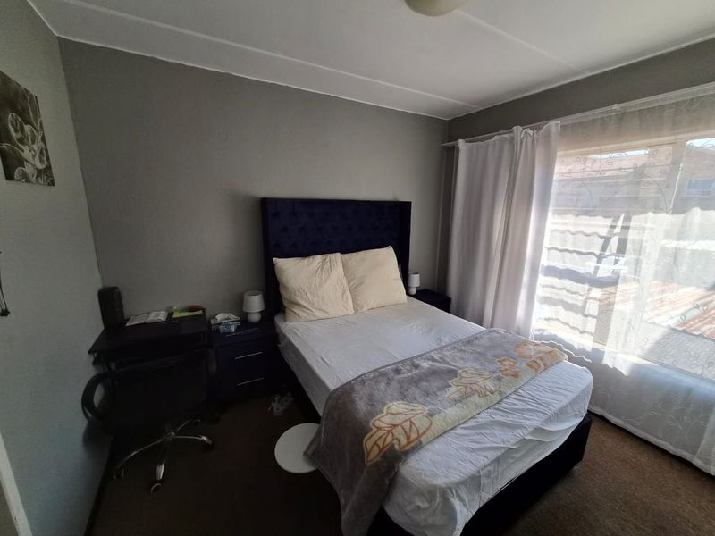 A functional bedroom featuring neutral wall finishes and natural light through a large window with installed curtain rails.