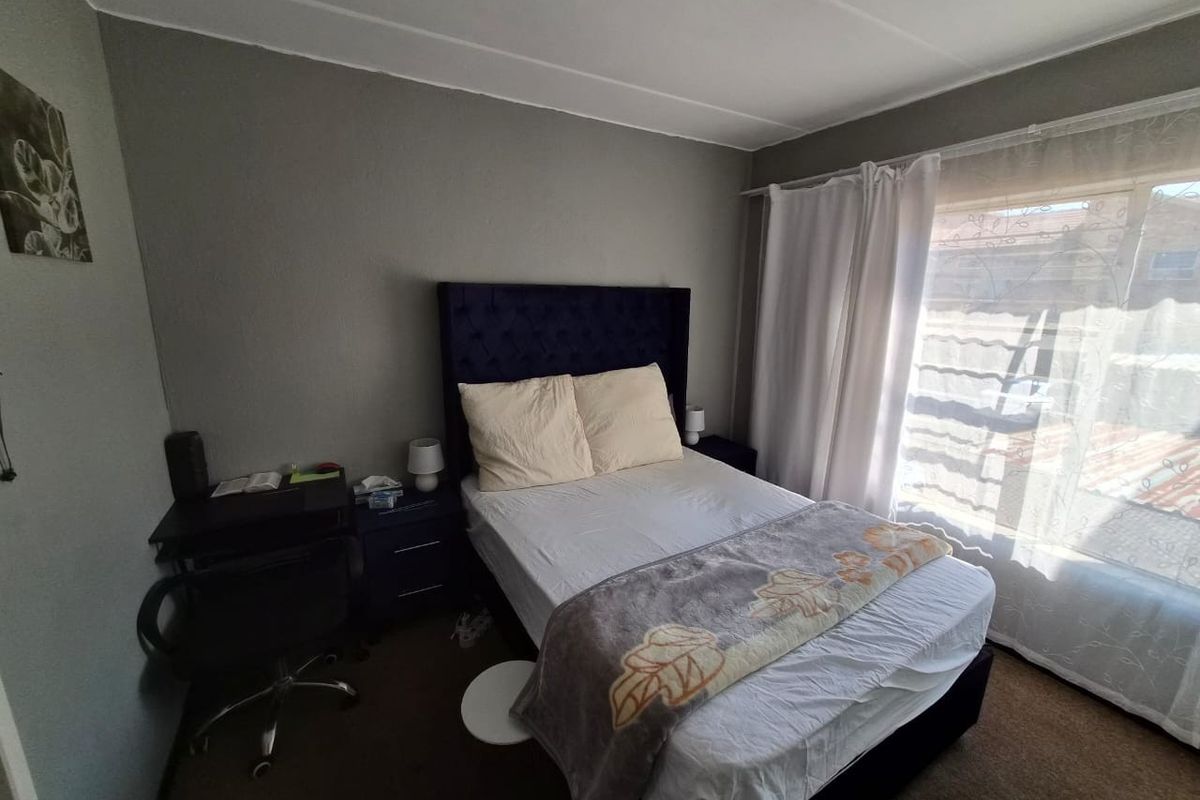 A functional bedroom featuring neutral wall finishes and natural light through a large window with installed curtain rails.