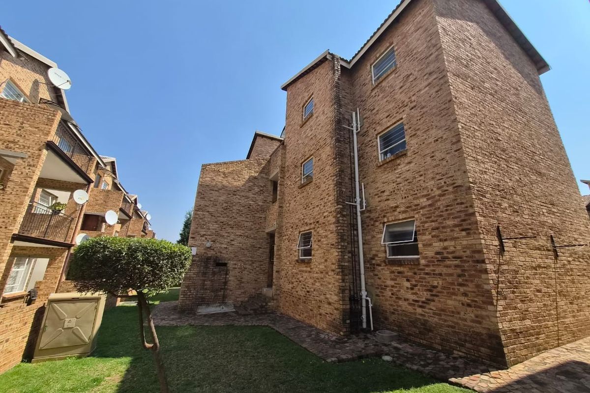Exterior view of a multi-story apartment building featuring face brick construction, paved walkways, and landscaped lawn areas.