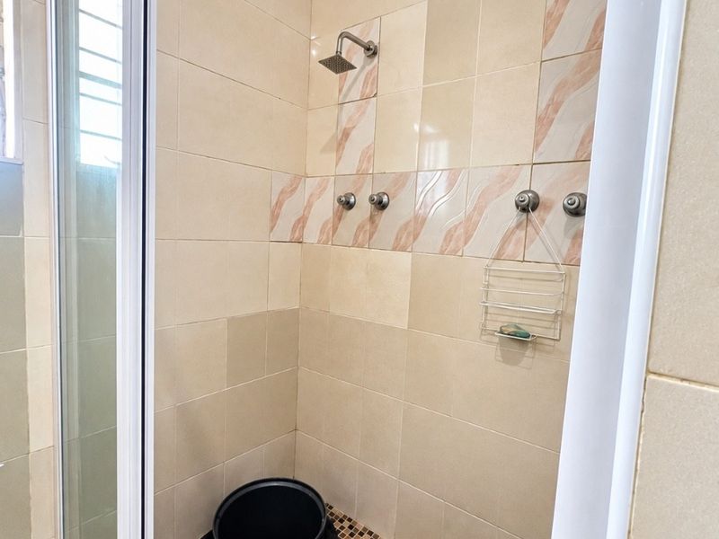 A functional shower enclosure featuring neutral wall tiles, mosaic floor tiling, and a fixed shower head with a glass screen.