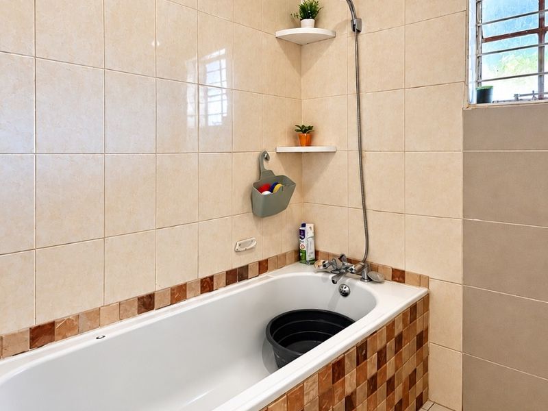 A functional bathroom featuring a bathtub with a handheld shower mixer, tiled walls, and a window with security bars.