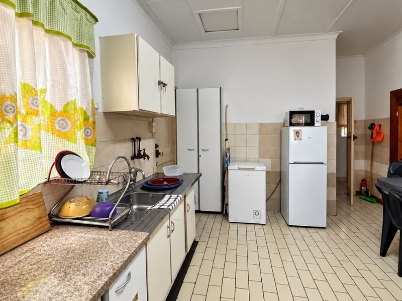A functional kitchen featuring laminate countertops, stainless steel sink, built-in cabinetry, and tiled flooring, offering potential for modernization and aesthetic updates.
