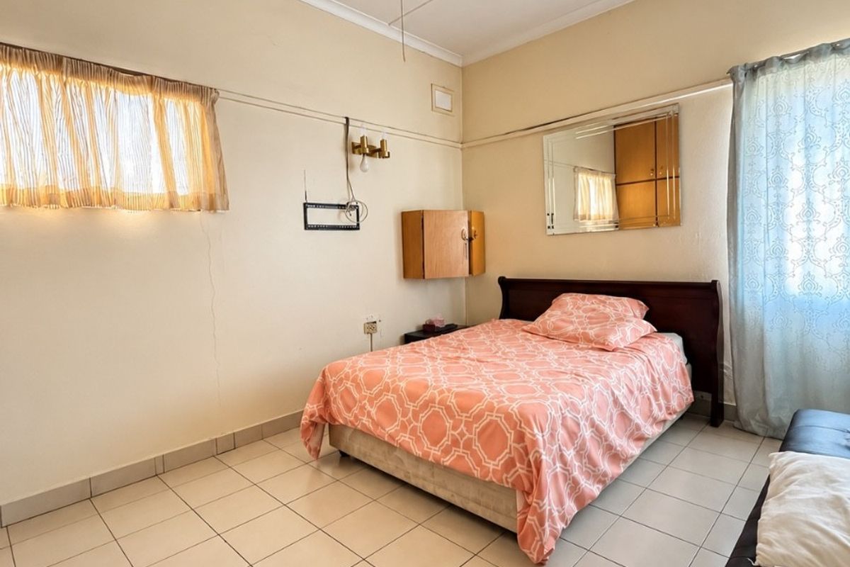 A bedroom featuring tiled flooring, a ceiling fan, and wall-mounted storage. The space shows signs of wear and requires cosmetic updates.