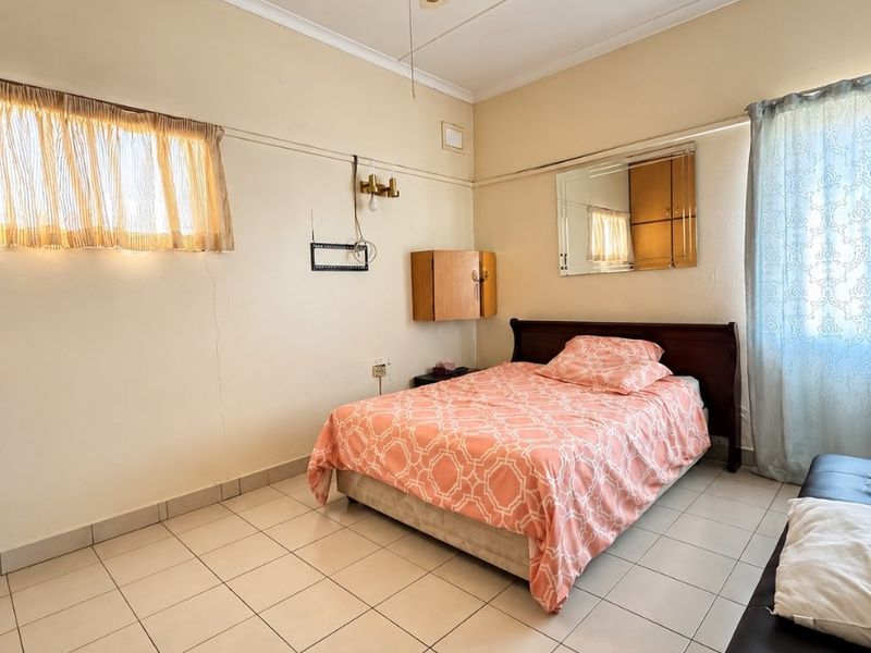 A bedroom featuring tiled flooring, a ceiling fan, and wall-mounted storage. The space shows signs of wear and requires cosmetic updates.