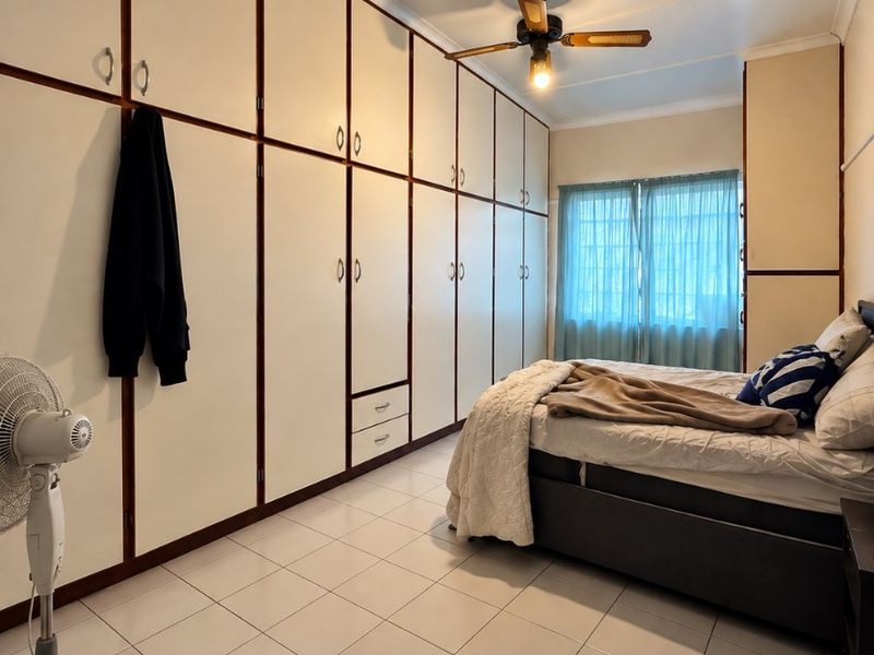 A bedroom featuring extensive floor-to-ceiling built-in cupboards, tiled flooring, and a ceiling fan, offering ample storage space.