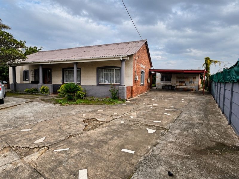 Front view of a single-story brick house featuring a large concrete driveway, attached carport, and perimeter boundary walling.