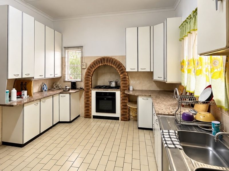 A functional kitchen featuring white cabinetry, laminate countertops, a unique brick arch oven surround, and durable ceramic floor tiles.