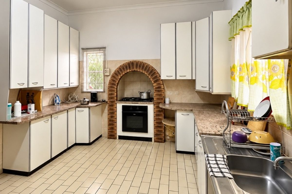 A functional kitchen featuring white cabinetry, laminate countertops, a unique brick arch oven surround, and durable ceramic floor tiles.