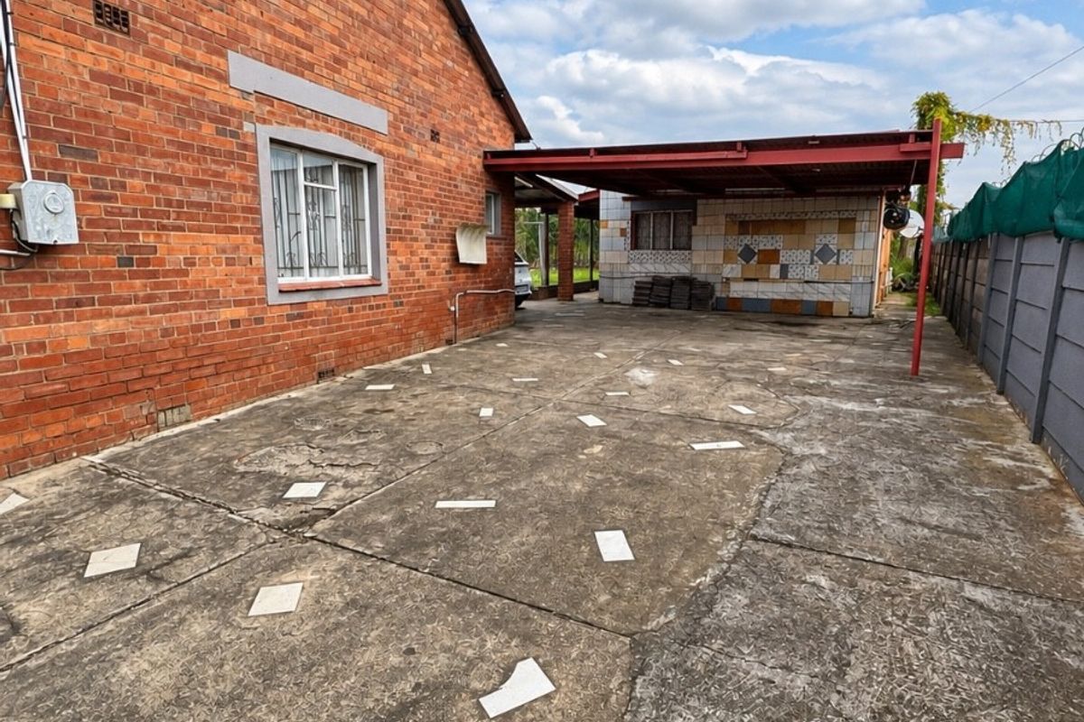 Rear exterior area featuring a large concrete driveway, covered patio structure, and perimeter walling, offering potential for outdoor renovation and landscaping.