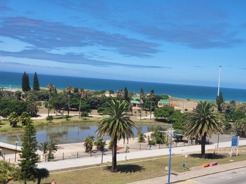 A scenic elevated view overlooking a coastal park, pond, and the ocean horizon.