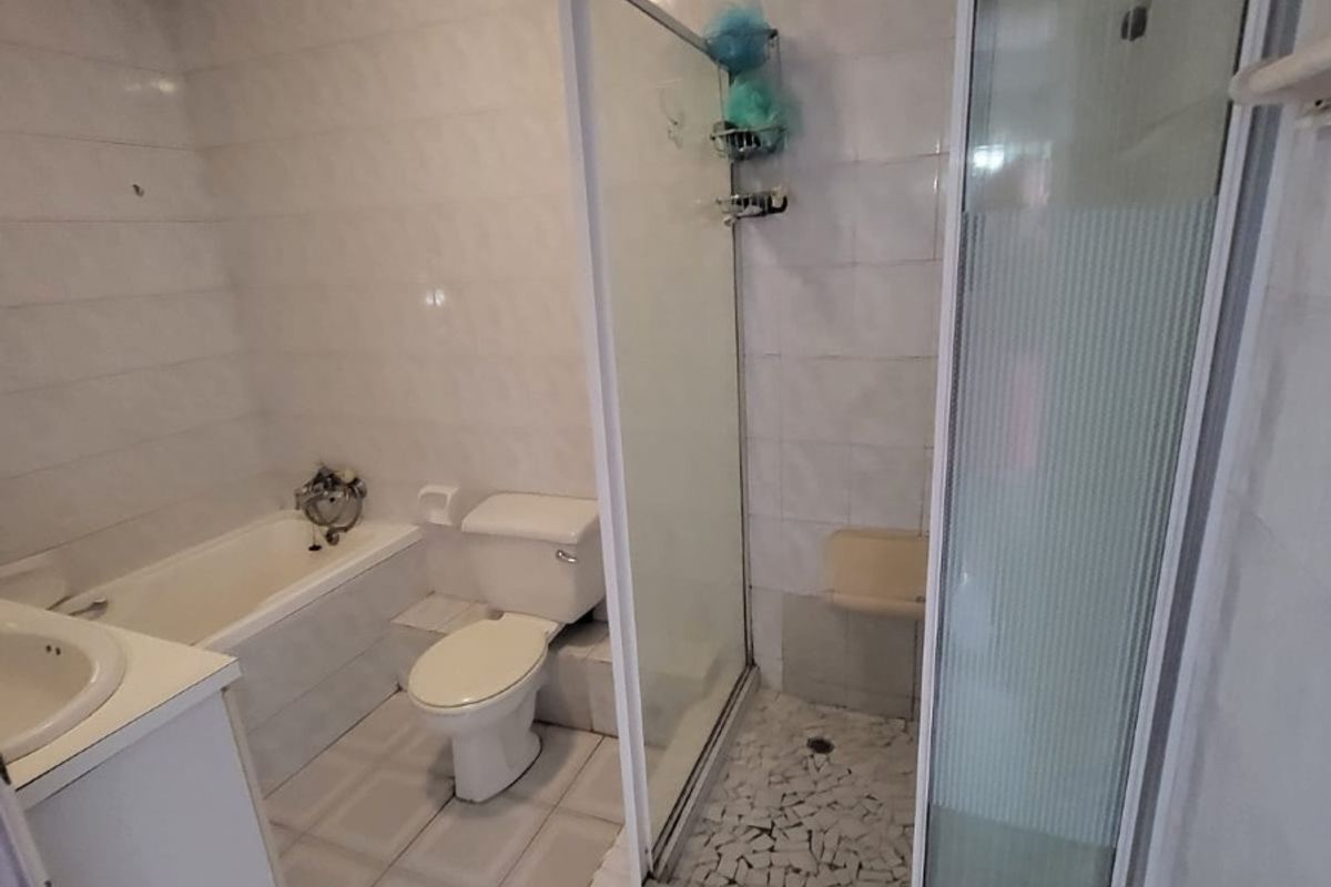A functional bathroom featuring a separate bathtub, shower enclosure, toilet, and vanity basin with neutral tiled finishes throughout.