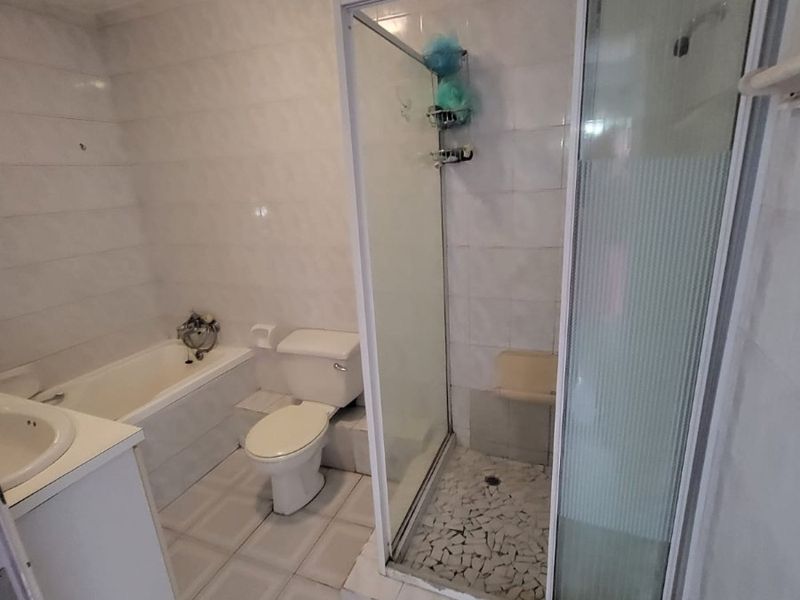 A functional bathroom featuring a separate bathtub, shower enclosure, toilet, and vanity basin with neutral tiled finishes throughout.
