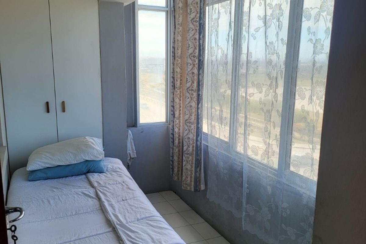 A compact bedroom featuring tiled flooring, a built-in wardrobe, and a large window providing natural light and exterior views.