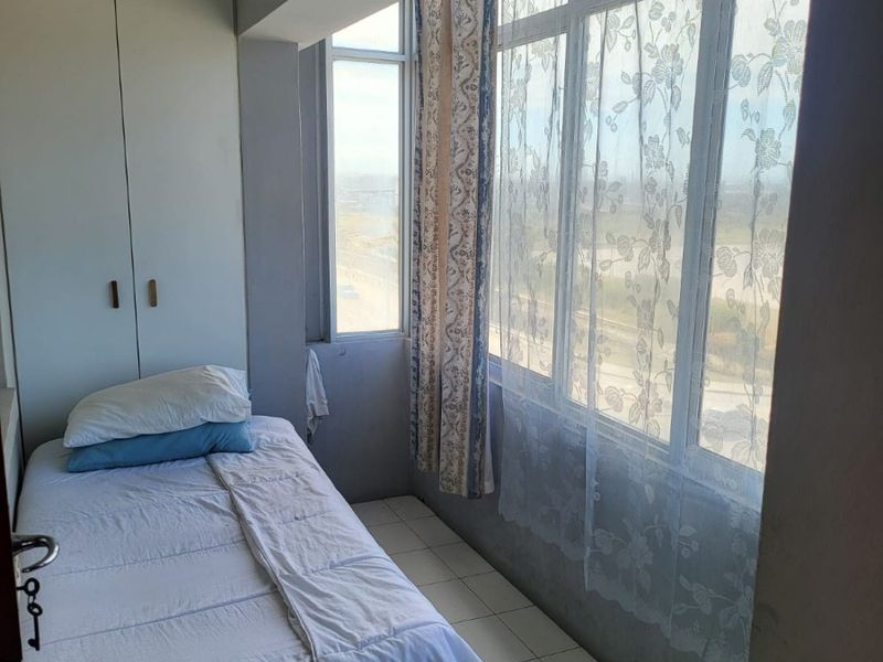 A compact bedroom featuring tiled flooring, a built-in wardrobe, and a large window providing natural light and exterior views.