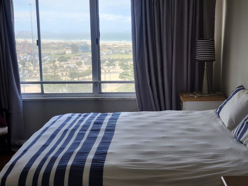 A bedroom featuring a large window with expansive coastal and city views, providing natural light and a scenic outlook.