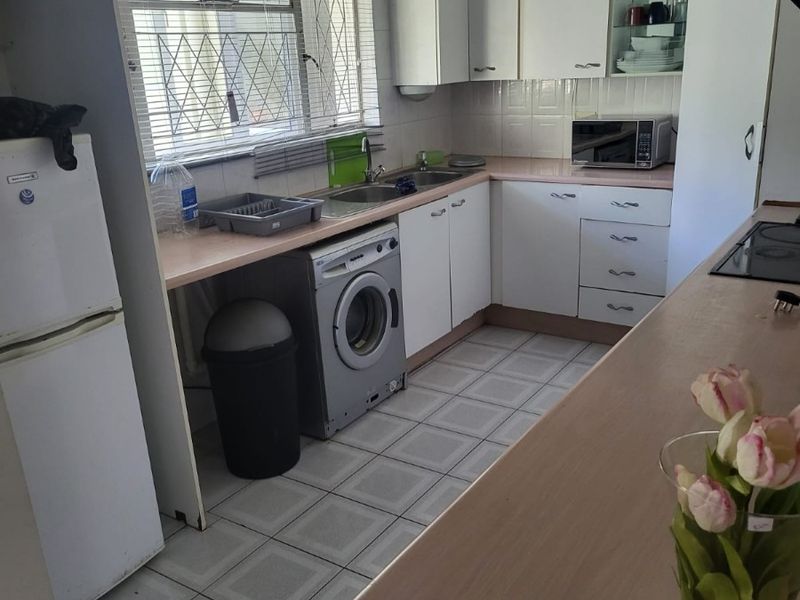 A functional kitchen featuring white built-in cabinetry, laminate countertops, a stainless steel sink, and tiled flooring, offering a practical layout for daily use.
