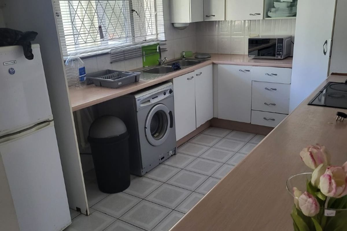 A functional kitchen featuring white built-in cabinetry, laminate countertops, a stainless steel sink, and tiled flooring, offering a practical layout for daily use.