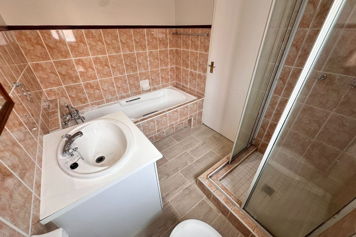 A functional bathroom featuring a built-in bathtub, separate shower enclosure, and a vanity basin with tiled finishes throughout.