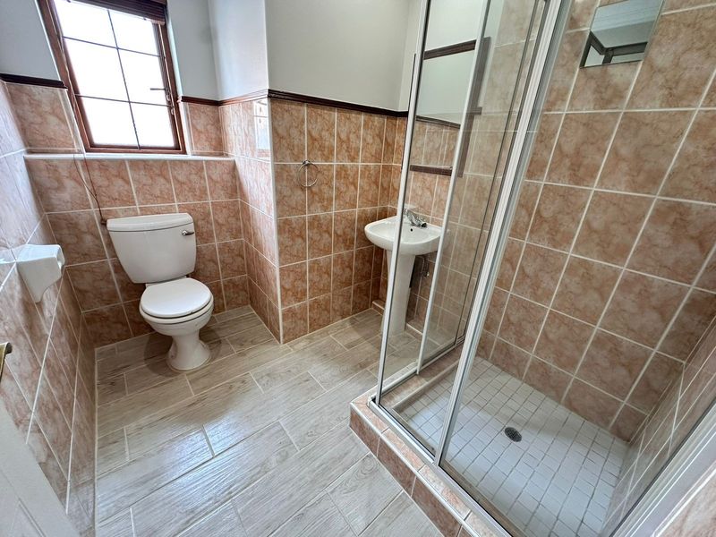 A functional bathroom featuring a shower enclosure, pedestal basin, and toilet, finished with neutral wall and floor tiling.