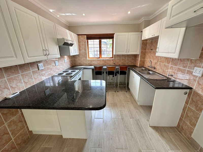 A well-maintained kitchen featuring granite countertops, ample built-in cabinetry, an electric hob with extractor, and a double sink with tiled backsplash.