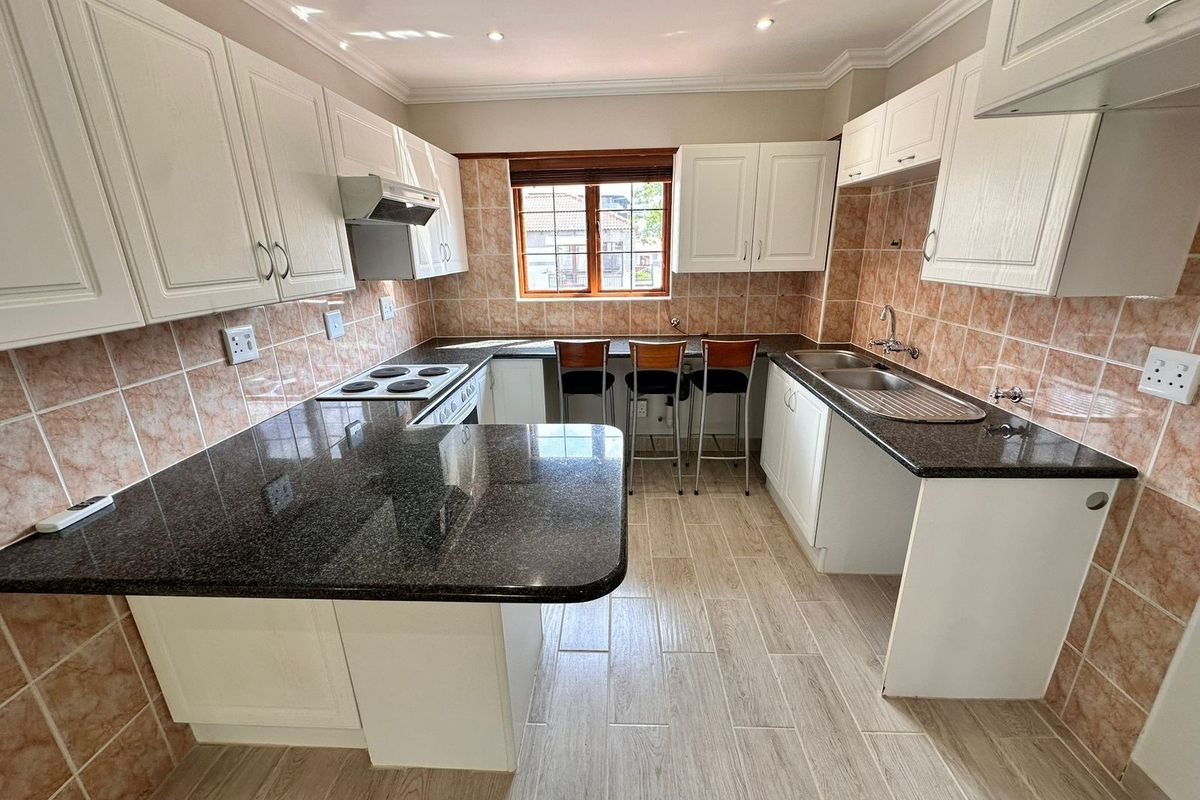 A well-maintained kitchen featuring granite countertops, ample built-in cabinetry, an electric hob with extractor, and a double sink with tiled backsplash.